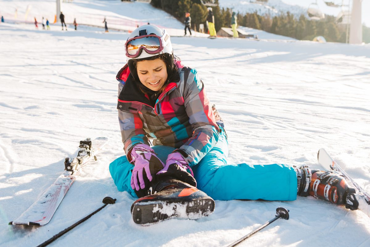 Teenage girl skiing in Italian Alps, sitting on snow and holding her injured leg. Winter, daytime. Sunny weather.