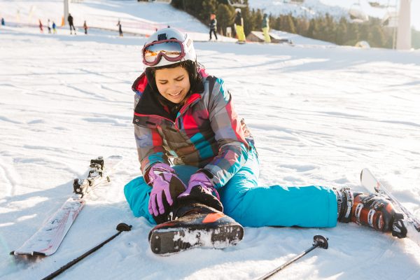 Teenage girl skiing in Italian Alps, sitting on snow and holding her injured leg. Winter, daytime. Sunny weather.